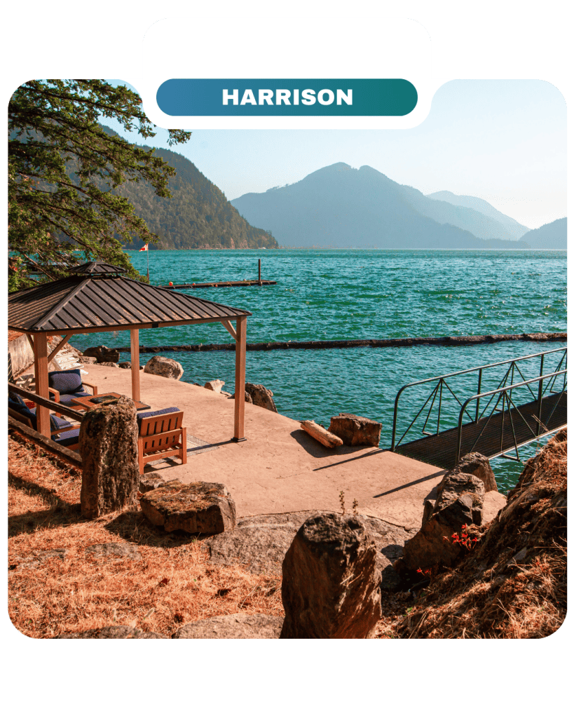 A lakeside patio with a gazebo, benches, and dock overlooks turquoise water and distant mountains under a clear sky at Harrison—perfect for relaxing and enjoying the Lifty Life.