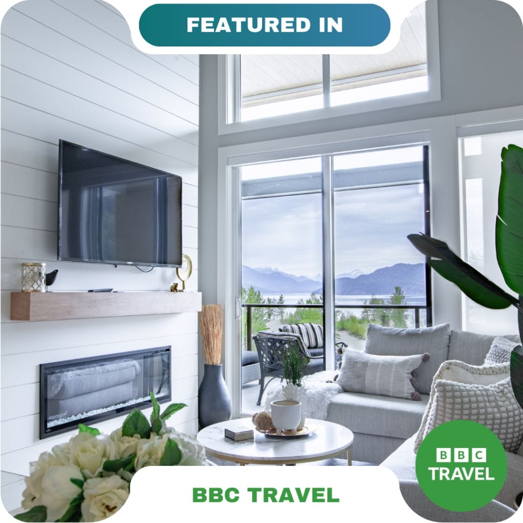Modern living room with large windows, a wall-mounted TV, fireplace, and neutral decor overlooking a scenic outdoor view—featured in BBC Travel and ideal for relaxing with partners.