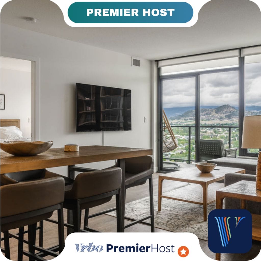 Modern living and dining area with wall-mounted TV, large windows, and balcony offering mountain and city views—perfect for partners; bedroom visible through an open doorway.