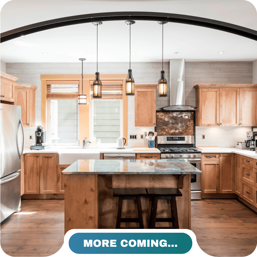 Modern kitchen with wooden cabinets, stainless steel appliances, an island with two stools, and pendant lights; perfect for vacation rentals in Cultus Lake. Text at bottom reads "MORE COMING…".