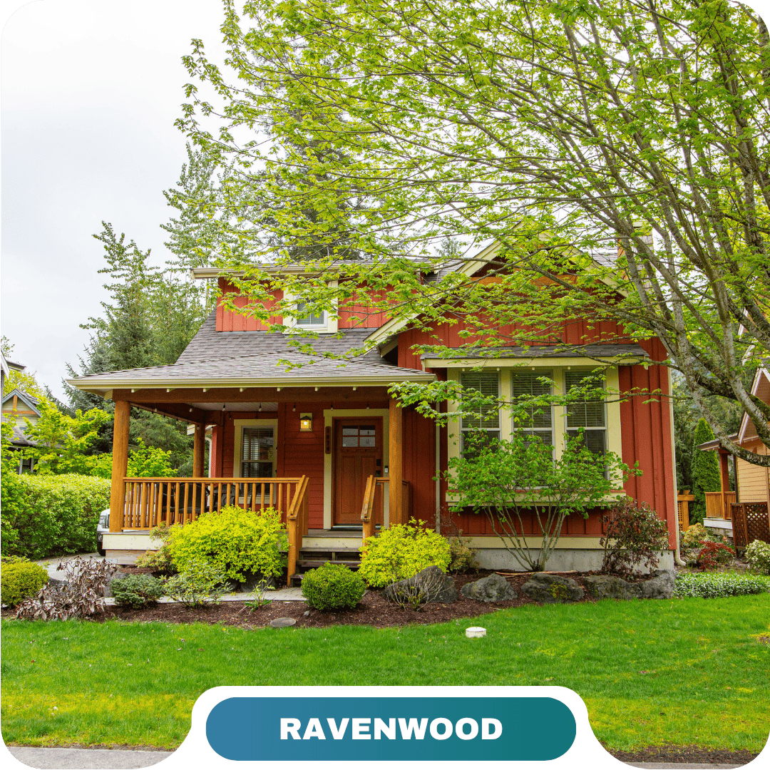 A two-story red house with a covered front porch, surrounded by green trees and shrubs, labeled "RAVENWOOD" at the bottom—ideal for vacation rentals in Cultus Lake.