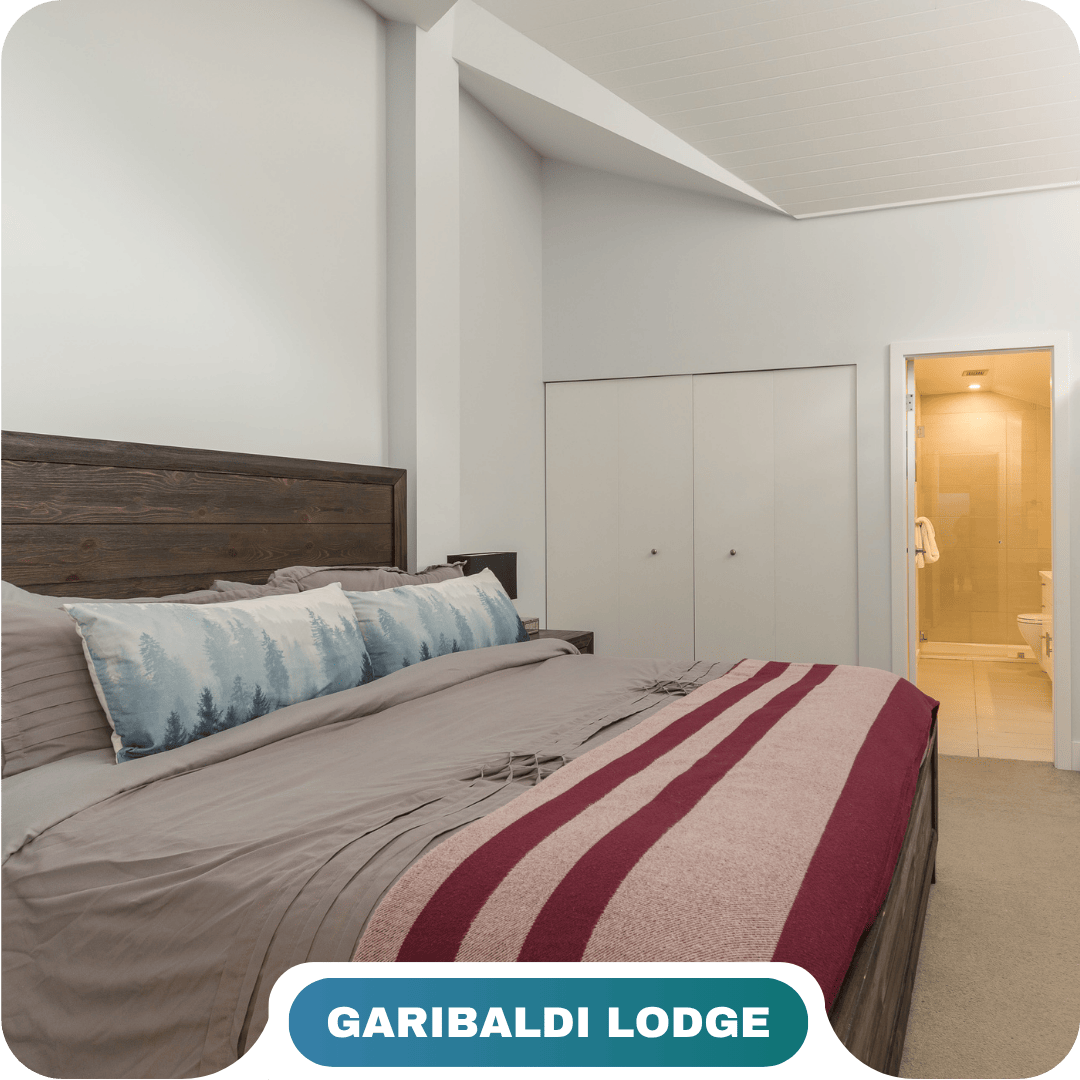A neatly made bed with tree-themed pillows and a red-striped blanket sits in a bedroom with white walls, a closet, and an ensuite bathroom—perfect for those seeking vacation rentals in Whistler. Text reads "GARIBALDI LODGE.