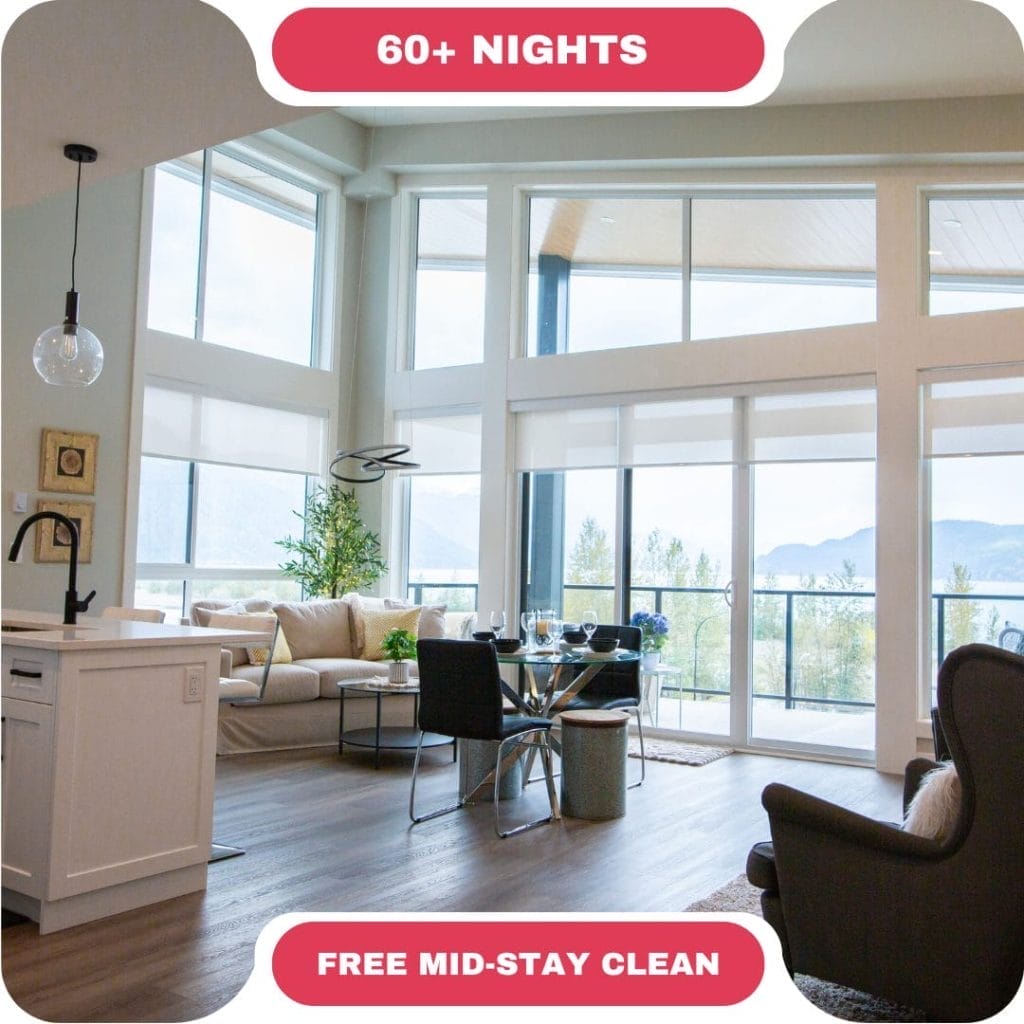 Modern living room with large windows, dining table, kitchen island, and mountain view. Enjoy exclusive deals on stays of 60+ nights, plus a free mid-stay clean.