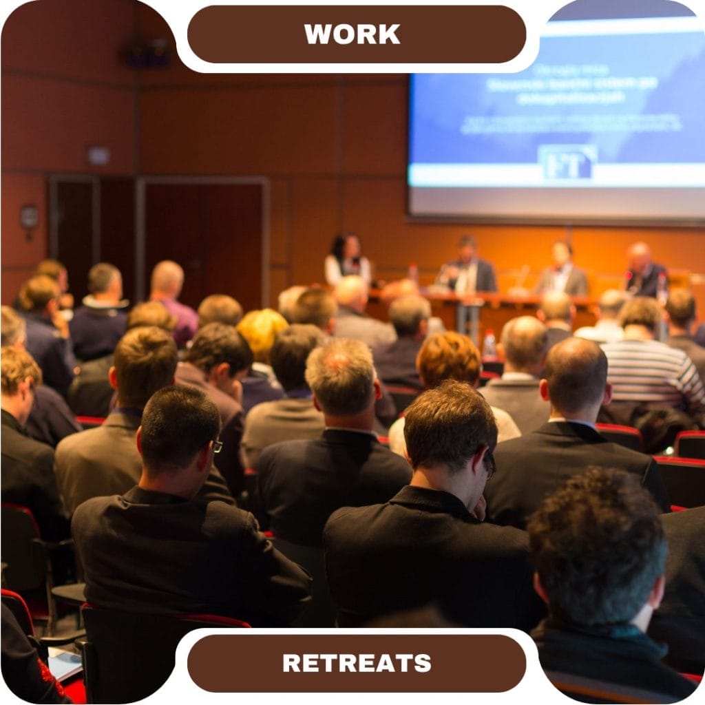 People attending a work retreat seminar in a conference room featuring furnished rentals, listening to speakers seated at a panel in front of a presentation screen.